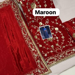 May include: Maroon fabric with gold floral embroidery and trim. The fabric appears to be velvet. The word "Maroon" is displayed in a white rectangular box. A small image of a person wearing a blue outfit is also visible.