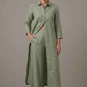 May include: A sage green long-sleeved button-down shirt dress with a classic collar and side slits, paired with matching wide-leg trousers. The ensemble features a textured fabric finish, a full-length front button placket, and neutral slip-on shoes.