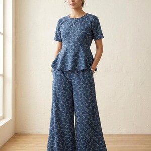 May include: A blue peplum top with short sleeves and a round neckline paired with matching wide-leg trousers. Both pieces feature a repeating white botanical leaf pattern throughout the fabric, creating a coordinated two-piece set.
