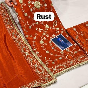 May include: Rust-coloured fabric with detailed gold embroidery, showcasing floral and vine designs. The fabric is presented with a matching border and a small image. The word "Rust" is displayed on the fabric.