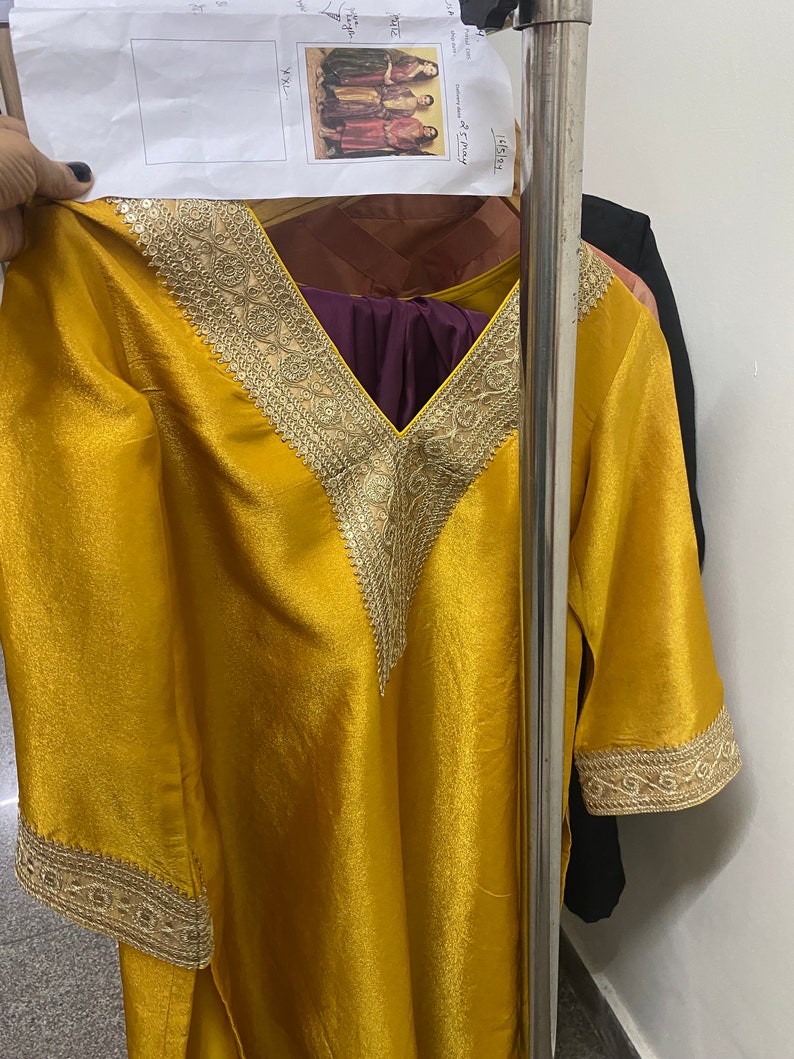 May include: A mustard yellow tunic with gold embroidery around the neckline and sleeves. The tunic has a V-neckline and is made of a silky fabric.