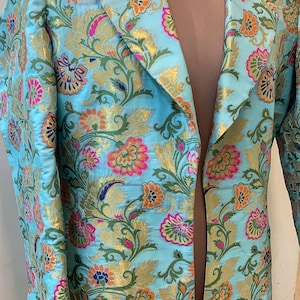 May include: A light blue blazer with a floral pattern in orange, pink, and gold. The jacket has a classic lapel and long sleeves. The floral design is a repeating pattern of stylized flowers and leaves.