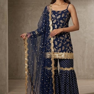 Peut inclure: Une tunique sans manches bleu marine avec des motifs de feuilles dor&eacute;es et un ourlet festonn&eacute;, associ&eacute;e &agrave; un pantalon large assorti &agrave; pois dor&eacute;s. Un dupatta bleu marine transparent avec des sequins dor&eacute;s et une bordure festonn&eacute;e compl&egrave;te l'ensemble.