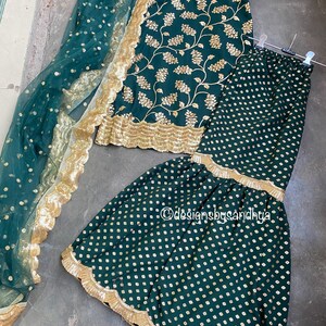 Peut inclure: Un ensemble haut sans manches et pantalon &eacute;vas&eacute; vert fonc&eacute; avec broderies florales dor&eacute;es et bordures &agrave; sequins festonn&eacute;es. Un dupatta vert fonc&eacute; transparent &agrave; pois dor&eacute;s et large bordure dor&eacute;e festonn&eacute;e est inclus. Texte designsbysandhya.