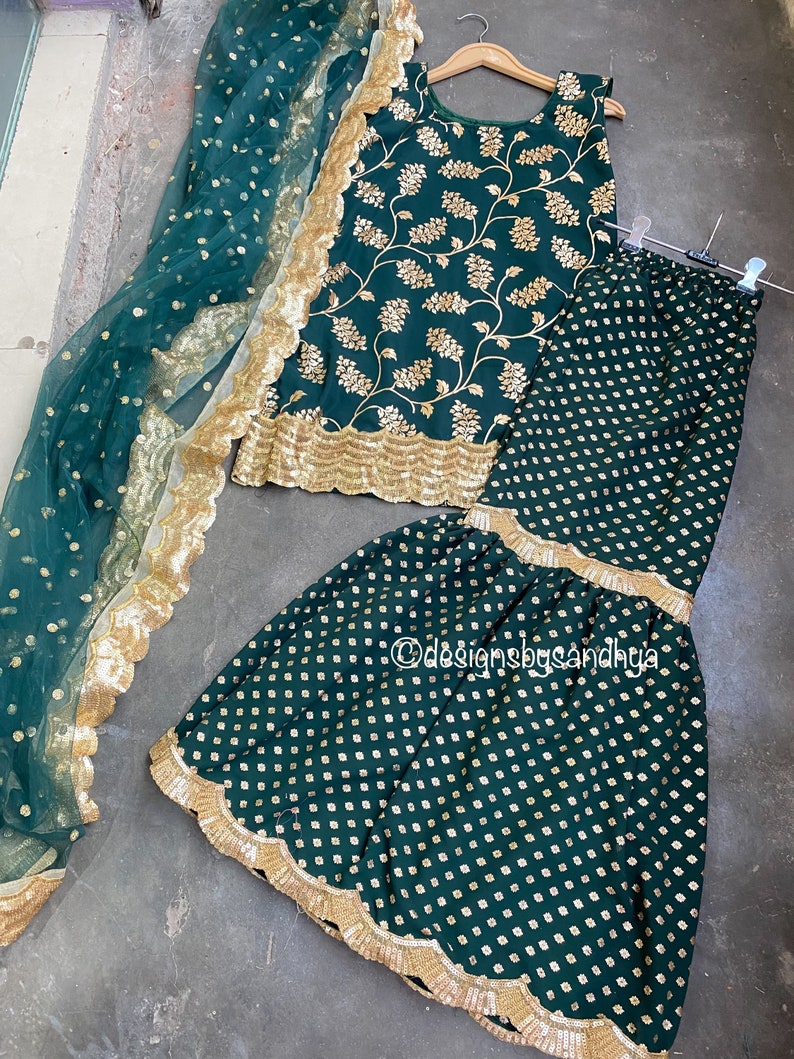 Peut inclure: Un ensemble haut sans manches et pantalon &eacute;vas&eacute; vert fonc&eacute; avec broderies florales dor&eacute;es et bordures &agrave; sequins festonn&eacute;es. Un dupatta vert fonc&eacute; transparent &agrave; pois dor&eacute;s et large bordure dor&eacute;e festonn&eacute;e est inclus. Texte designsbysandhya.
