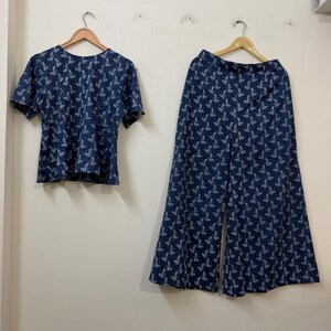 May include: A two-piece set consisting of a short-sleeved top and wide-leg trousers. Both garments are made from a dark blue fabric featuring a repeating white botanical leaf pattern. The top has a round neckline, and the trousers have a high waist.