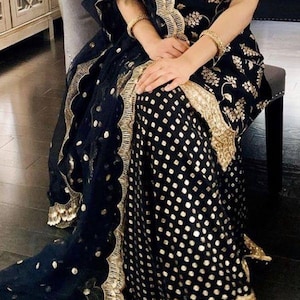 Peut inclure: Un ensemble sans manches bleu marine fonc&eacute; compos&eacute; d'un haut et d'un pantalon large, orn&eacute; de broderies florales dor&eacute;es sur le corsage et d'un motif g&eacute;om&eacute;trique dor&eacute; sur le pantalon. Un dupatta bleu marine transparent avec bordure dor&eacute;e.