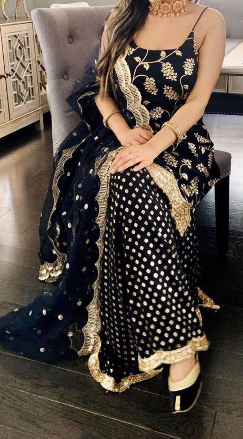 Peut inclure: Un ensemble sans manches bleu marine fonc&eacute; compos&eacute; d'un haut et d'un pantalon large, orn&eacute; de broderies florales dor&eacute;es sur le corsage et d'un motif g&eacute;om&eacute;trique dor&eacute; sur le pantalon. Un dupatta bleu marine transparent avec bordure dor&eacute;e.