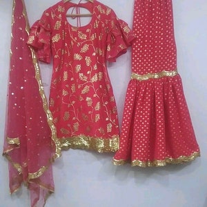 Peut inclure: Un ensemble trois pi&egrave;ces rose vif compos&eacute; d'une tunique &agrave; manches &agrave; volants avec des motifs floraux dor&eacute;s, d'une jupe &eacute;vas&eacute;e assortie &agrave; ourlet dor&eacute; et d'une dupatta rose transparente avec des paillettes dor&eacute;es et une bordure festonn&eacute;e.