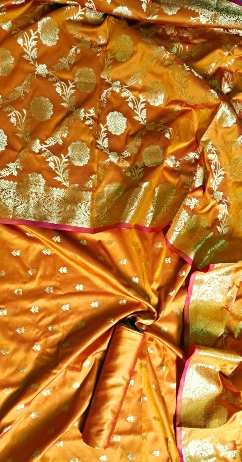 May include: A golden yellow silk saree with a floral pattern in gold and silver thread. The saree has a pink and gold border.