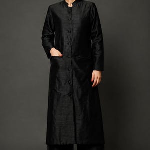 May include: A long-sleeved black tunic with a mandarin collar, a full-length button-down front, and two side pockets, paired with matching wide-leg trousers. The ensemble is crafted from a textured fabric and worn with red embroidered flat shoes.