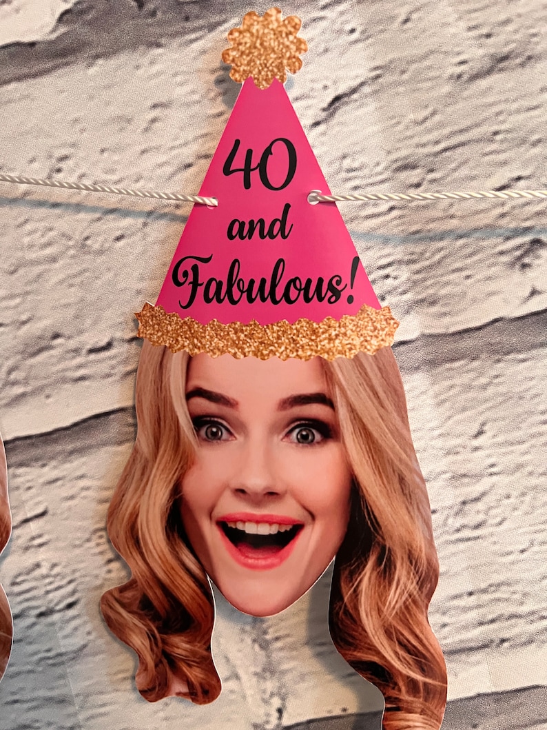 Pink and gold party banner with the text "40 and Fabulous!" on each end. The banner features a pink party hat with gold glitter and a woman's face with blonde hair.