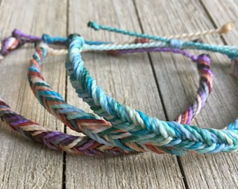 May include: Three braided bracelets in a variety of colors, including blue, green, purple, and orange. The bracelets are made of woven string and are stacked on top of each other.