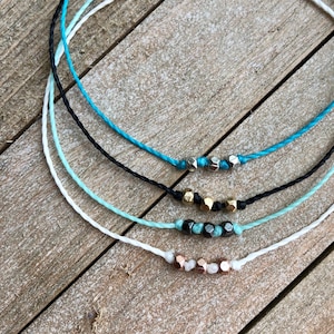 May include: Four colourful bracelets with different coloured beads. The bracelets are made of thin string and have a variety of beads, including silver, gold, and rose gold.