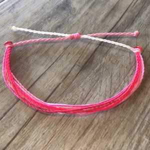 May include: A pink and white friendship bracelet with a knotted design.