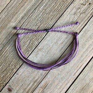 May include: A purple and brown braided bracelet with a simple knot closure.