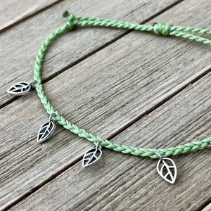 May include: A green braided cord bracelet with four silver leaf charms.