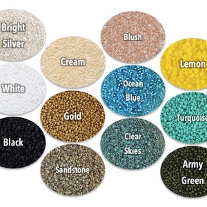 May include: A collection of small, colorful beads in various shades, including bright silver, cream, gold, black, and army green. Each color is displayed in a separate oval, with the color name printed above. The beads are likely for jewelry making or crafts.