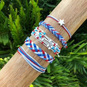 Puede incluir: Conjunto de cinco pulseras de amistad de color rojo, blanco y azul. Las pulseras están hechas de cuerda trenzada y cuentas. Una pulsera tiene un dije de estrella plateada.