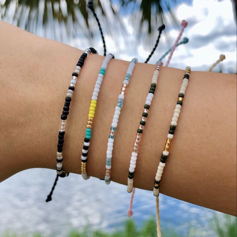 Puede incluir: Un conjunto de seis pulseras de cuentas coloridas con diferentes patrones. Las pulseras est&aacute;n hechas con cuentas peque&ntilde;as en negro, blanco, dorado, turquesa y amarillo.