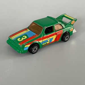 May include: Green toy car with a yellow, blue, and red racing stripe. The car has the number "3" on the side and the word "UNILOP" printed on it.