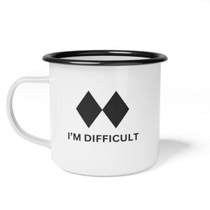 May include: White enamel mug with a black rim and handle. The mug features two black diamond shapes and the text "I'M DIFFICULT" in black. A humorous and bold statement for tea or coffee.