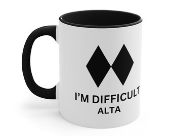 May include: White ceramic coffee mug with a black rim and handle. The mug features a black diamond symbol and the text "I'M DIFFICULT ALTA".