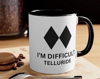 May include: White coffee mug with a black rim and handle. The mug has a black diamond logo and the text "I'm Difficult Telluride".
