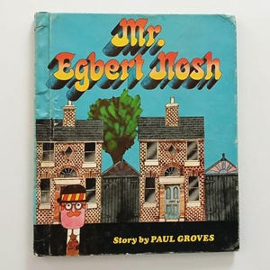 May include: A children's book titled Mr. Egbert Nosh with a story by Paul Groves. The cover features a light blue background, two brick houses, a green tree, and a cartoon character wearing a hat and glasses, all rendered in a colorful illustration.
