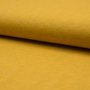Könnte beinhalten: Nahaufnahme eines weichen, gelben Stoffes mit einer dezenten Textur. Der Stoff ist in der Mitte gefaltet und zeigt die glatte Oberfläche und die texturierte Seite.