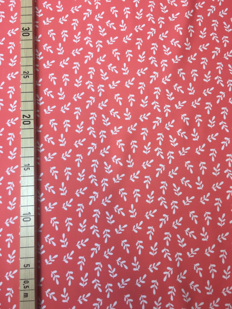 May include: Coral fabric with a white leaf pattern. The fabric is measured in inches.