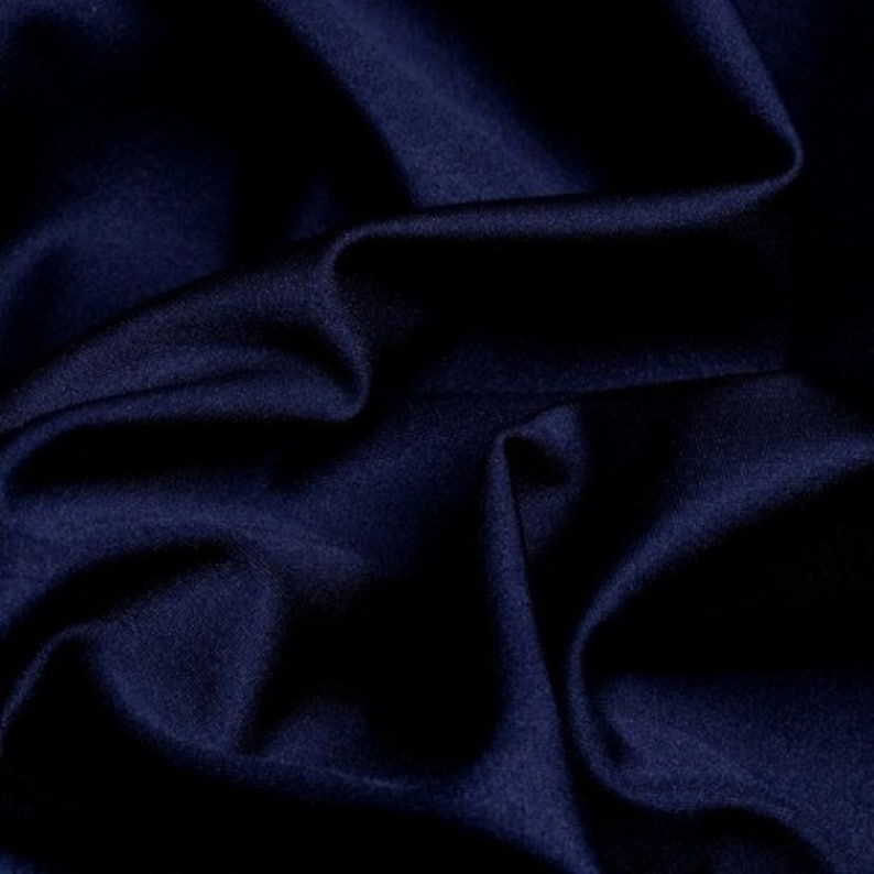 Puede incluir: Un primer plano de una tela azul oscuro con una textura suave y sedosa. La tela est&aacute; drapeada y doblada, creando l&iacute;neas suaves y fluidas.