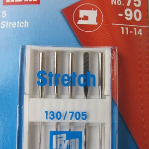 Könnte beinhalten: Eine Packung mit fünf silbernen Nähmaschinennadeln mit der Aufschrift "Stretch" in den Größen 75 und 90. Die Packung ist blau und weiß mit dem Prym-Logo und dem Text "130/705".