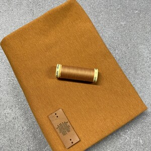 Könnte beinhalten: Ein braunes Stoffmuster mit einem kleinen braunen Leder-Etikett mit der Aufschrift "MADE IN ITALY" und einer Spule braunen Garns.