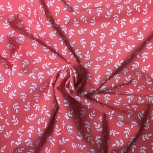 May include: Coral pink fabric with a white leaf pattern. The fabric is folded and textured.