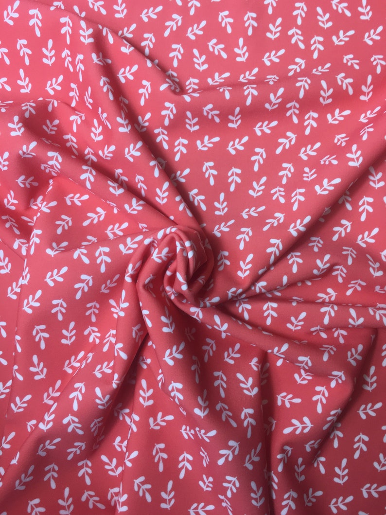 May include: Coral pink fabric with a white leaf pattern. The fabric is folded and textured.