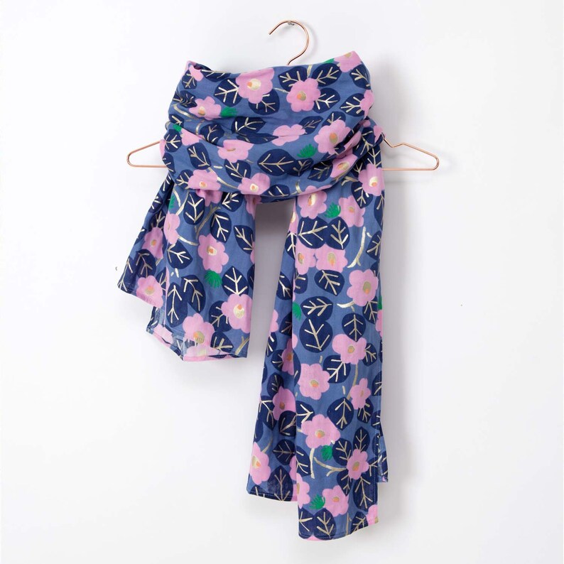 Puede incluir: Una bufanda azul con un estampado floral rosa y detalles dorados. La bufanda est&aacute; colgada de una percha.