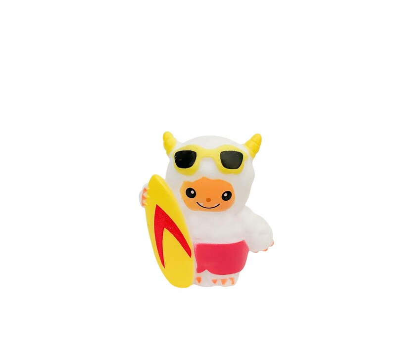Puede incluir: Una figura blanca de dibujos animados con cuernos amarillos y gafas de sol, sosteniendo una tabla de surf amarilla con un dise&ntilde;o rojo. La figura lleva pantalones cortos rojos y tiene una cara naranja. El tema general es un juguete divertido con tem&aacute;tica de playa.