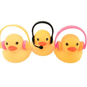 May include: Three yellow rubber duck toys, each with a different colored headset. One duck has a black headset with a microphone, while the others have pink and yellow headsets. All have orange beaks and black eyes.