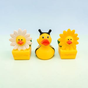 May include: Three yellow rubber duck toys. One duck is designed as a bee, and the other two are designed as flowers. The flower ducks have white and yellow petals. All three ducks have black eyes and red beaks.