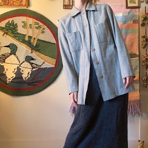 May include: A light gray long-sleeved shirt with a button-up front and two large pockets. The shirt is worn over a dark gray skirt.