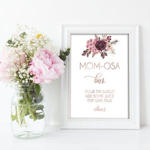 May include: A printable sign for a "Mom-osa Bar" with a floral design in shades of pink and purple. The sign says "Pour the bubbly, add some juice, top with fruit, cheers!"