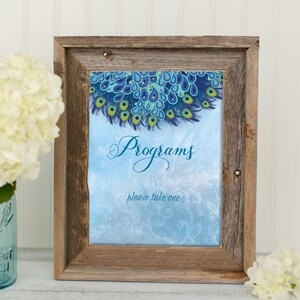 Könnte beinhalten: Ein rustikaler Holzrahmen mit einem Design aus blauen und grünen Pfauenfedern. Das Schild lautet "Programme, bitte nehmen Sie eins".