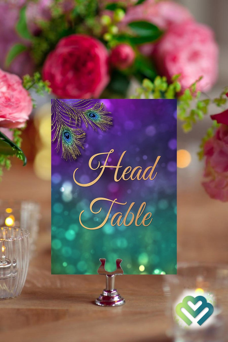 May include: A purple and teal table number card with gold glitter and peacock feathers. The card says "Head Table" in gold lettering.