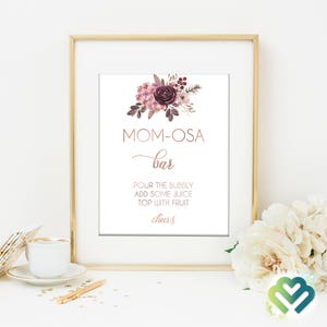 May include: A printable sign with a floral design in shades of pink and purple. The sign reads "MOM-OSA bar" and includes instructions for making a mimosa: "Pour the bubbly, add some juice, top with fruit, cheers."