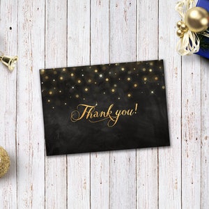 May include: A black card with gold glitter and the text "Thank you!" on a white wood background.