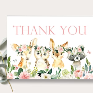 May include: Thank you card with a watercolor illustration of a deer, owl, bunny, and raccoon wearing floral crowns. The animals are surrounded by pink and white flowers and greenery.