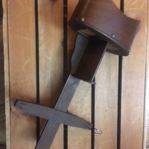May include: A vintage stereoscope viewer with a dark brown leather eye cup and a dark grey metal frame. The viewer is angled, showing its design and construction. The background is a wooden crate.