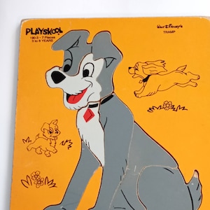 May include: Vintage Playskool wooden puzzle featuring Tramp from Disney's Lady and the Tramp. The puzzle has a yellow background with a gray and white dog, a running dog, and two small puppies. The puzzle is for ages 3 to 8 years.