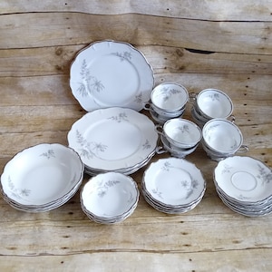May include: A set of white porcelain dinnerware with a silver trim and a floral design. The set includes dinner plates, salad plates, bowls, and teacups.